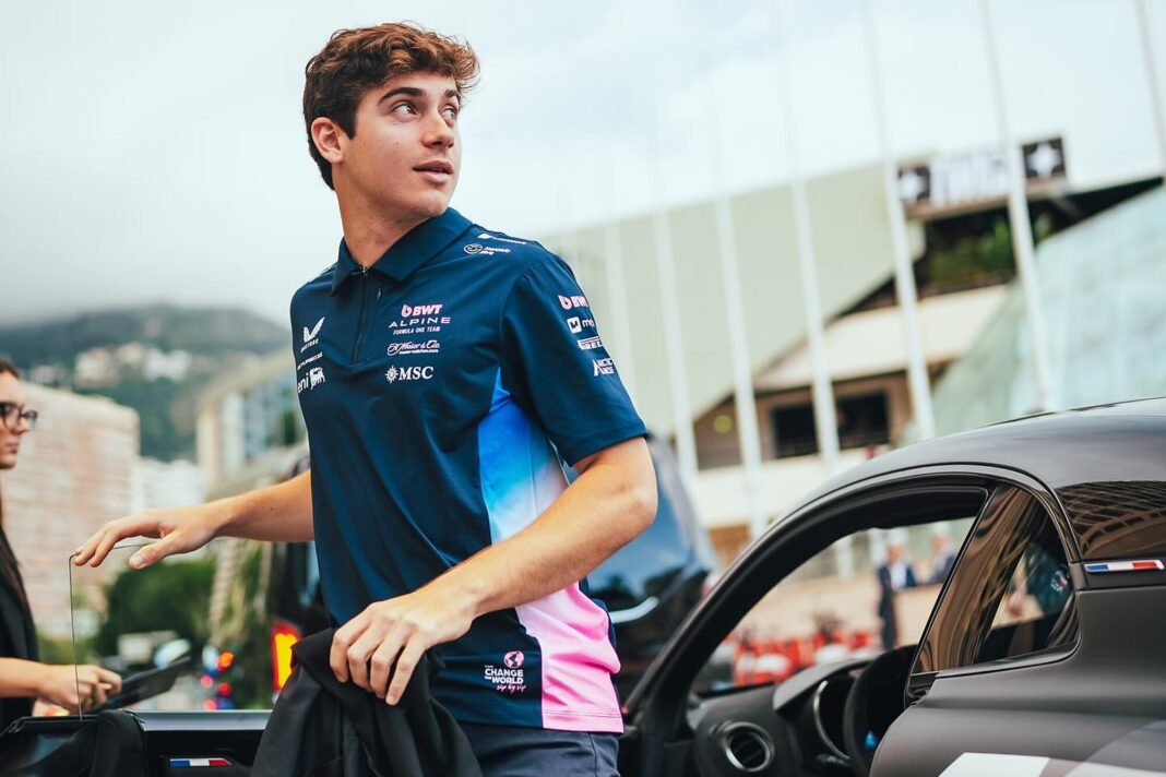 Grupo de personas viendo una carrera de Fórmula 1 en una pantalla gigante dentro de un local con simuladores de conducción.