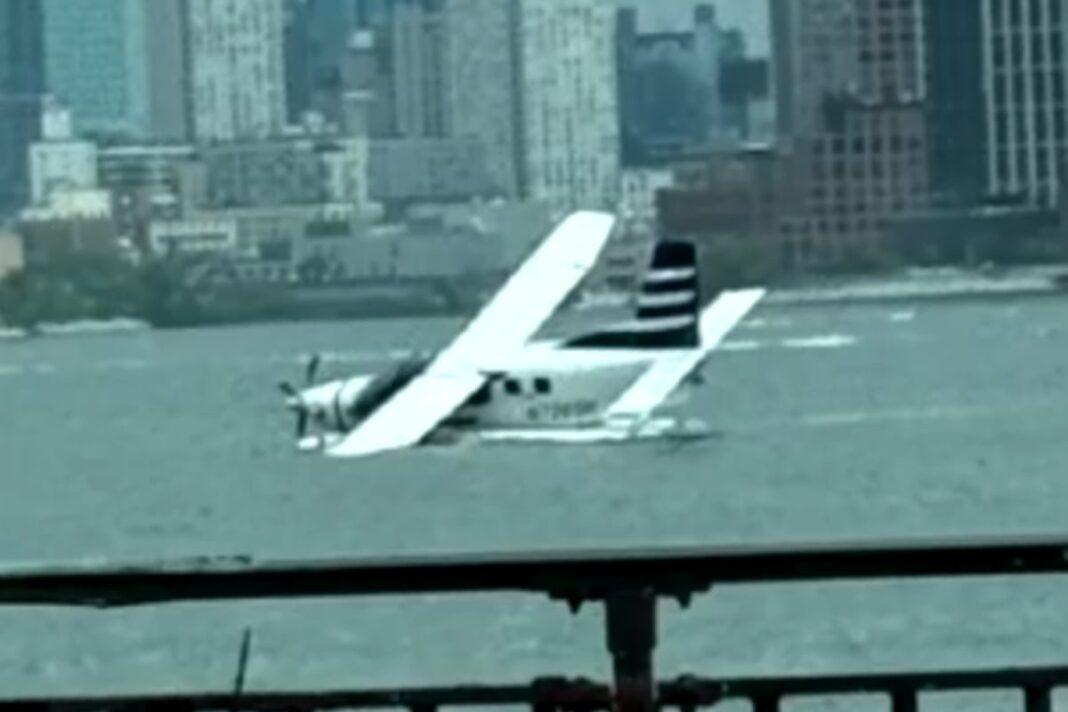 Hidroavión blanco escorado en el East River con un helicóptero sobrevolando