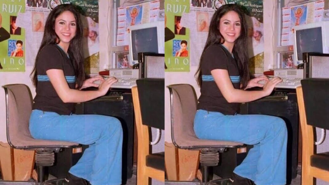 Shakira posando sentada en un escritorio, recreando la fotografía de 1997